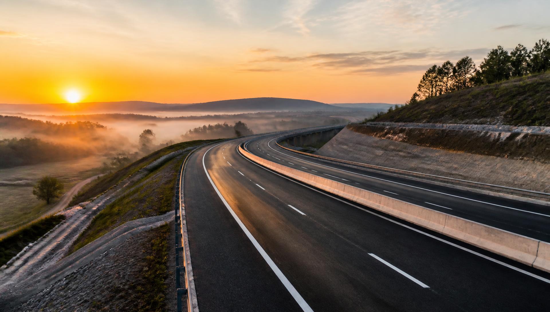 New highway curving through misty terrain at dawn